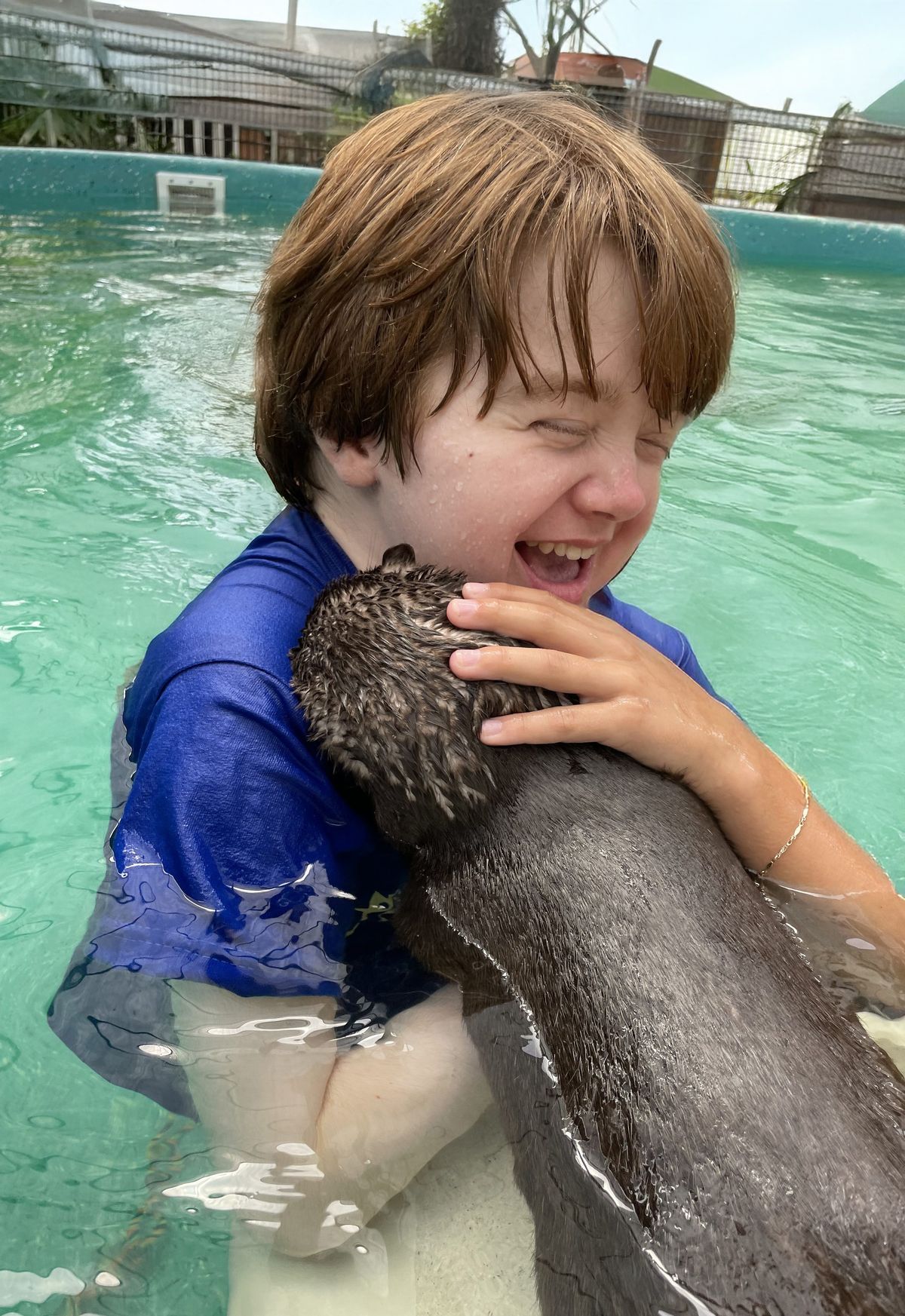 A child laughing while cradling an otter in the heated pool