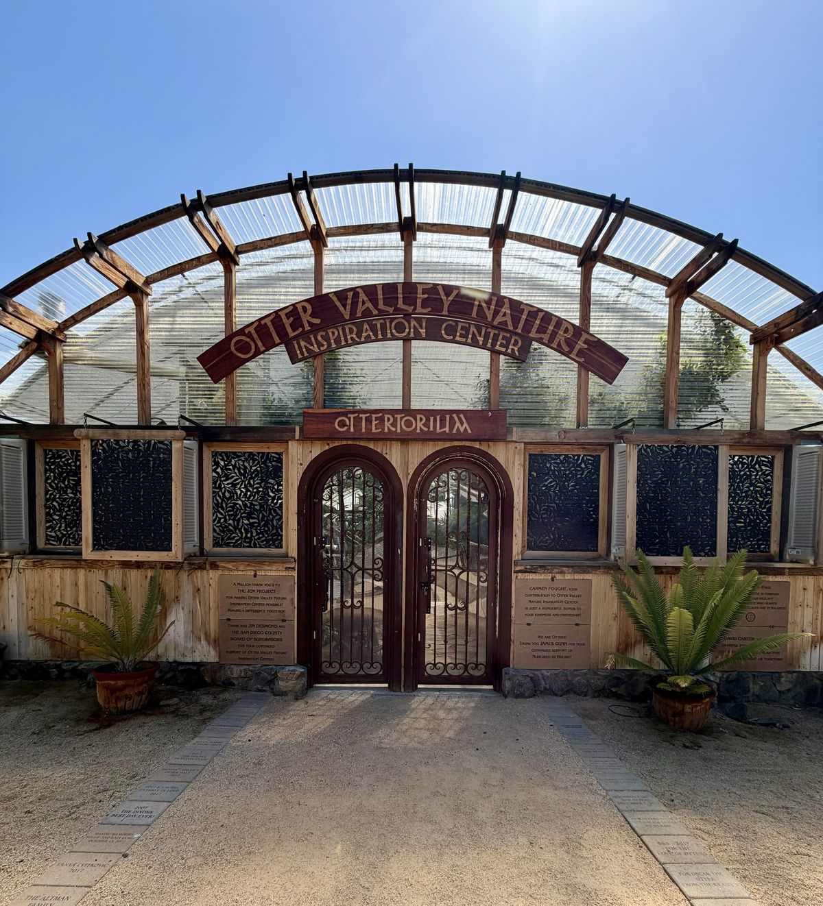 The arched wooden Ottertorium entrance, signed Otter Valley Nature Inspiration Center, with potted ferns and donor pavers along the path